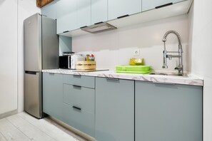 Une cuisine moderne équipée d’un réfrigérateur encastré, d’un four à micro-ondes, d’un évier avec un robinet et d’un plan de travail sur lequel se trouve un égouttoir vert.