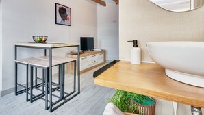 Una habitación moderna con una mesa de comedor de madera, un lavamanos blanco, un televisor y un cuadro en la pared.