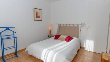Een slaapkamer met een bed, een hanglamp, een nachtkastje, een blauwe kleerhanger en een deur.