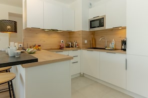 A modern kitchen with white cabinets, a wooden countertop, a microwave, a sink, and a dining area with stools.
