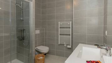 Ein Badezimmer mit einer gläsernen Duschkabine, einem weißen Waschbecken und einer Toilette.