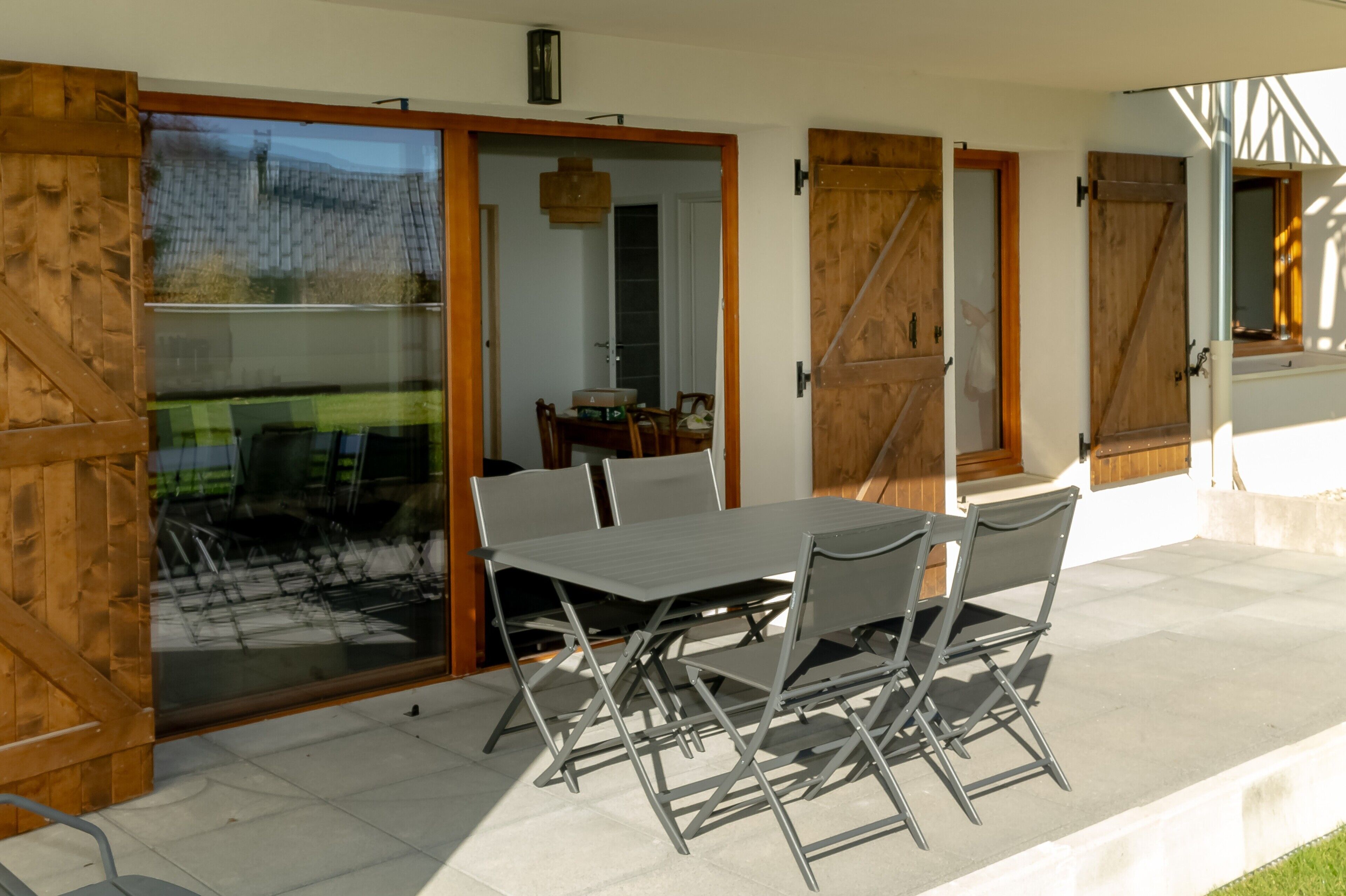 Eine Terrasse mit Tisch und Stühlen, Glastüren zum Verschieben und Blick auf ein grünes Feld.