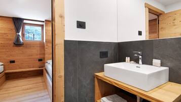 Un baño moderno con un lavamanos grande de color blanco, suelo de madera y una ventana con vistas.
