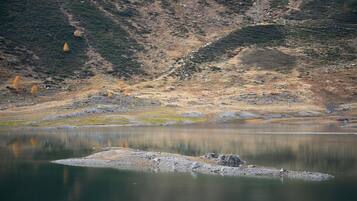 Ein ruhiger See mit steiniger Uferlinie und einem Bergpanorama im Hintergrund.