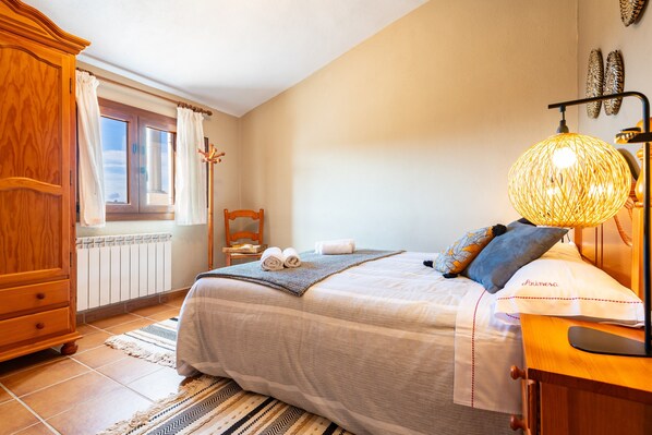 A bedroom with a bed, a wooden wardrobe, a window with curtains, a bedside table with a lamp, and a wall-mounted shelf. - Rural House 'Masia Arinesa - Cullatur' with Mountain Views, Private Terrace and Wi-Fi (Culla)