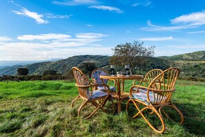 An outdoor dining area with wicker chairs and a table, set against a backdrop of green hills and a clear sky. - Rural House 'Masia Arinesa - Cullatur' with Mountain Views, Private Terrace and Wi-Fi (Culla)