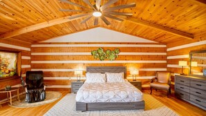 Ein Schlafzimmer in einer Blockhütte mit einem Bett, zwei Nachttischen, einem Sessel, einer Kommode und einem Deckenventilator.