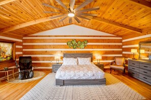 A log cabin bedroom with a bed, two bedside tables, a chair, a dresser, and a ceiling fan. - Tall Maple Lodge with Views (North Wilkesboro)