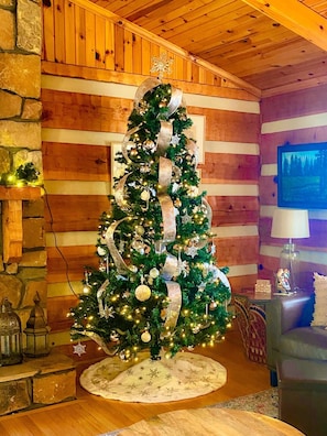 Un sapin de Noël dans une pièce rustique aux murs en bois et à la cheminée en pierre.