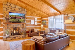 Ein Blockhaus-Interieur mit Kamin aus Stein, Ledersofa, Holzwänden und einem an der Wand befestigten Fernseher.