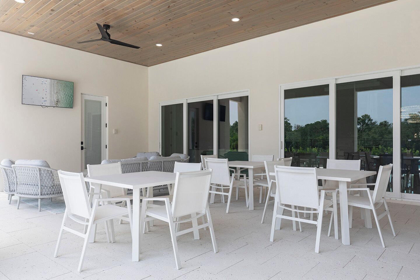 A spacious patio area with white furniture, large sliding glass doors, and a ceiling fan.