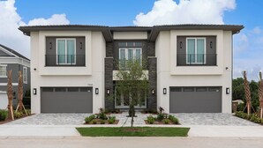 A modern two-story house with a central entrance, two garages, and a well-maintained front yard with a small tree and shrubs. - The Commodious Chateau-TT452 (Kissimmee)
