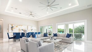 A spacious living room with a large sectional sofa, a dining area with blue chairs, and a ceiling fan. - The Commodious Chateau-TT452 (Kissimmee)