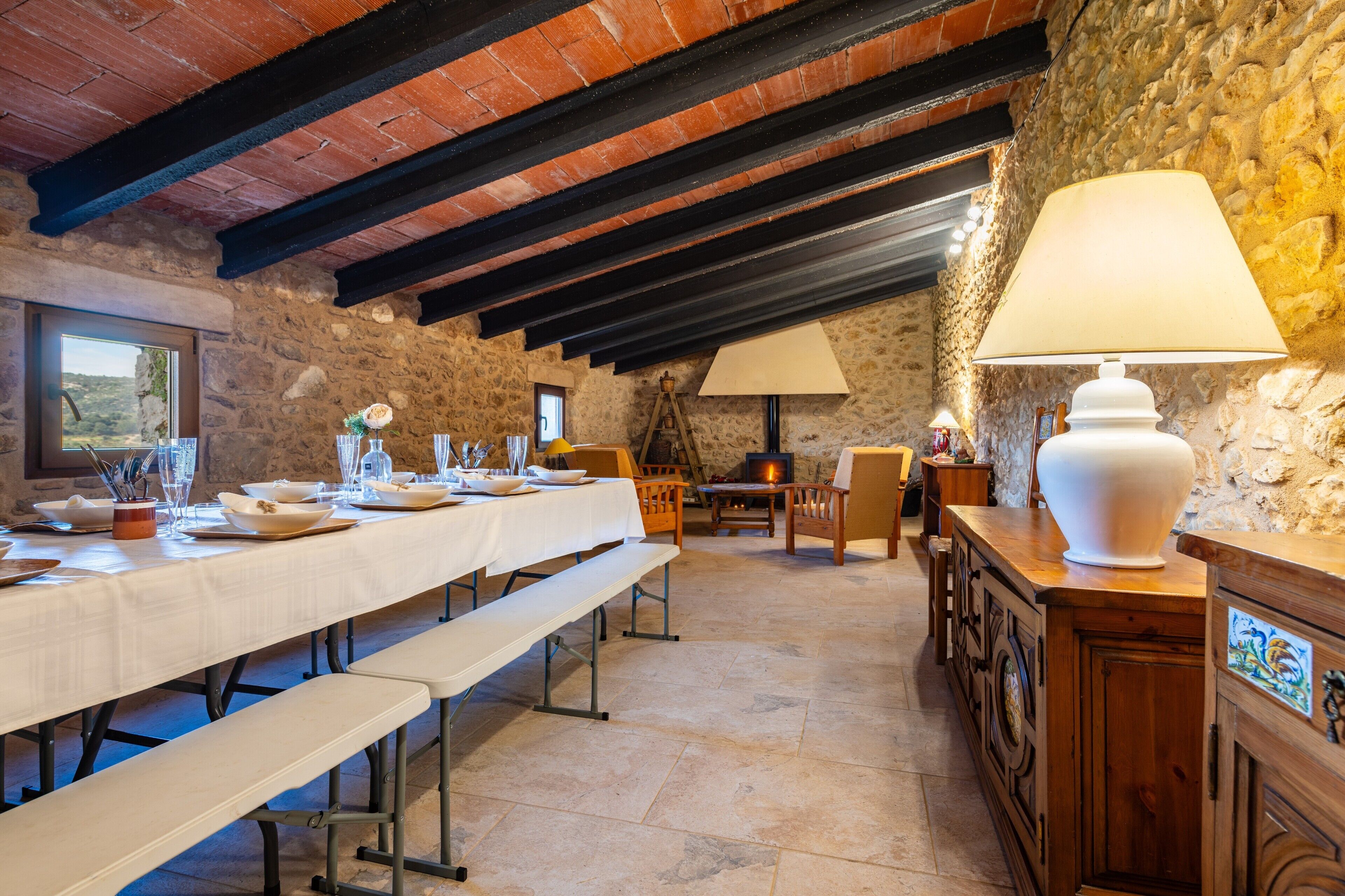 Un comedor rústico con una mesa larga dispuesta para una comida, paredes de piedra y vigas de madera a la vista.
