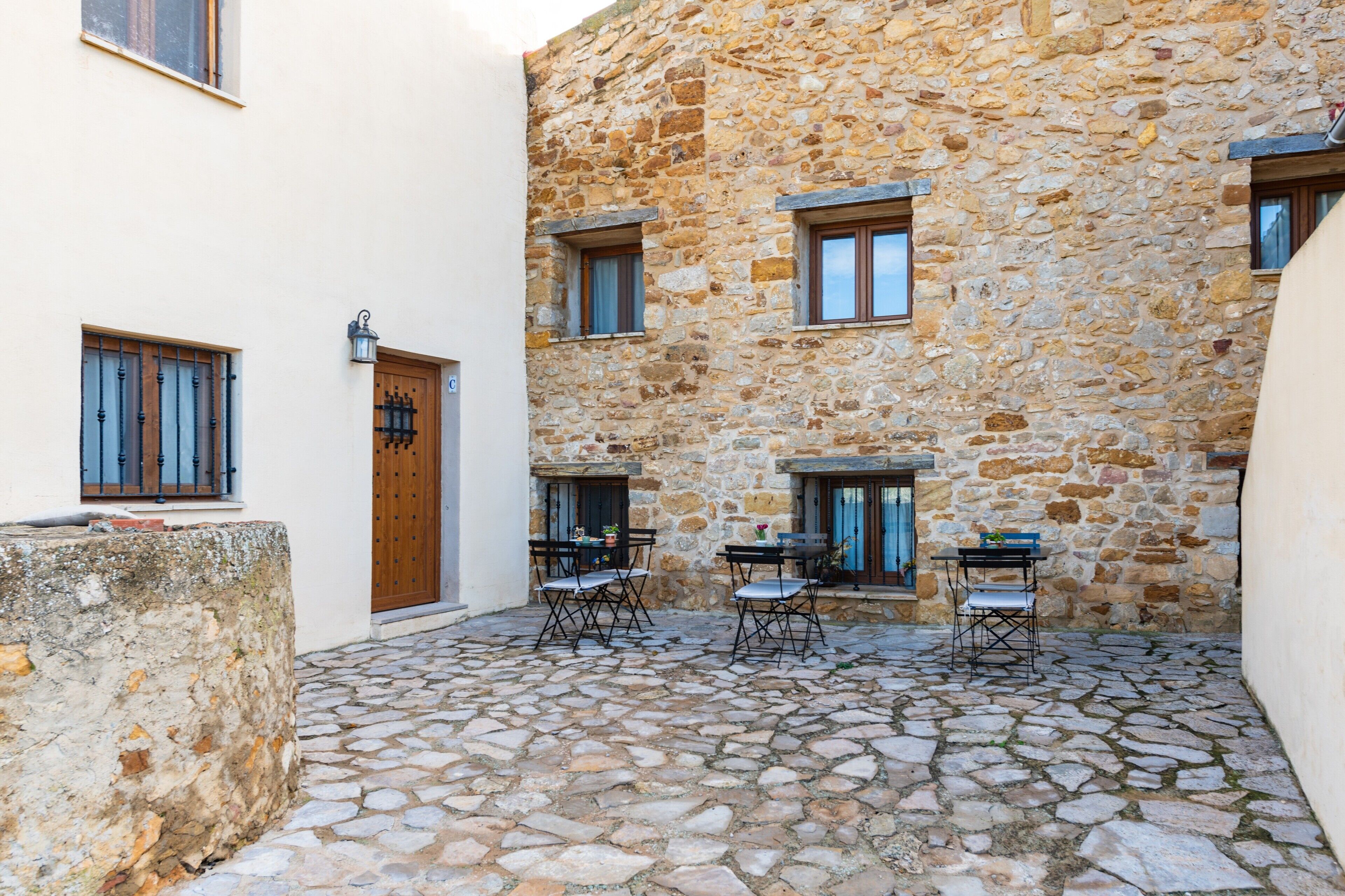 Un patio con suelo de piedra, una puerta de madera y dos mesas con sillas.