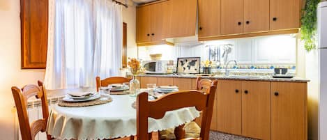 Ein Essbereich mit einem Tisch für vier Personen, Holzsessel, eine Küche mit Holzschränken, einer Mikrowelle und einem Kühlschrank.