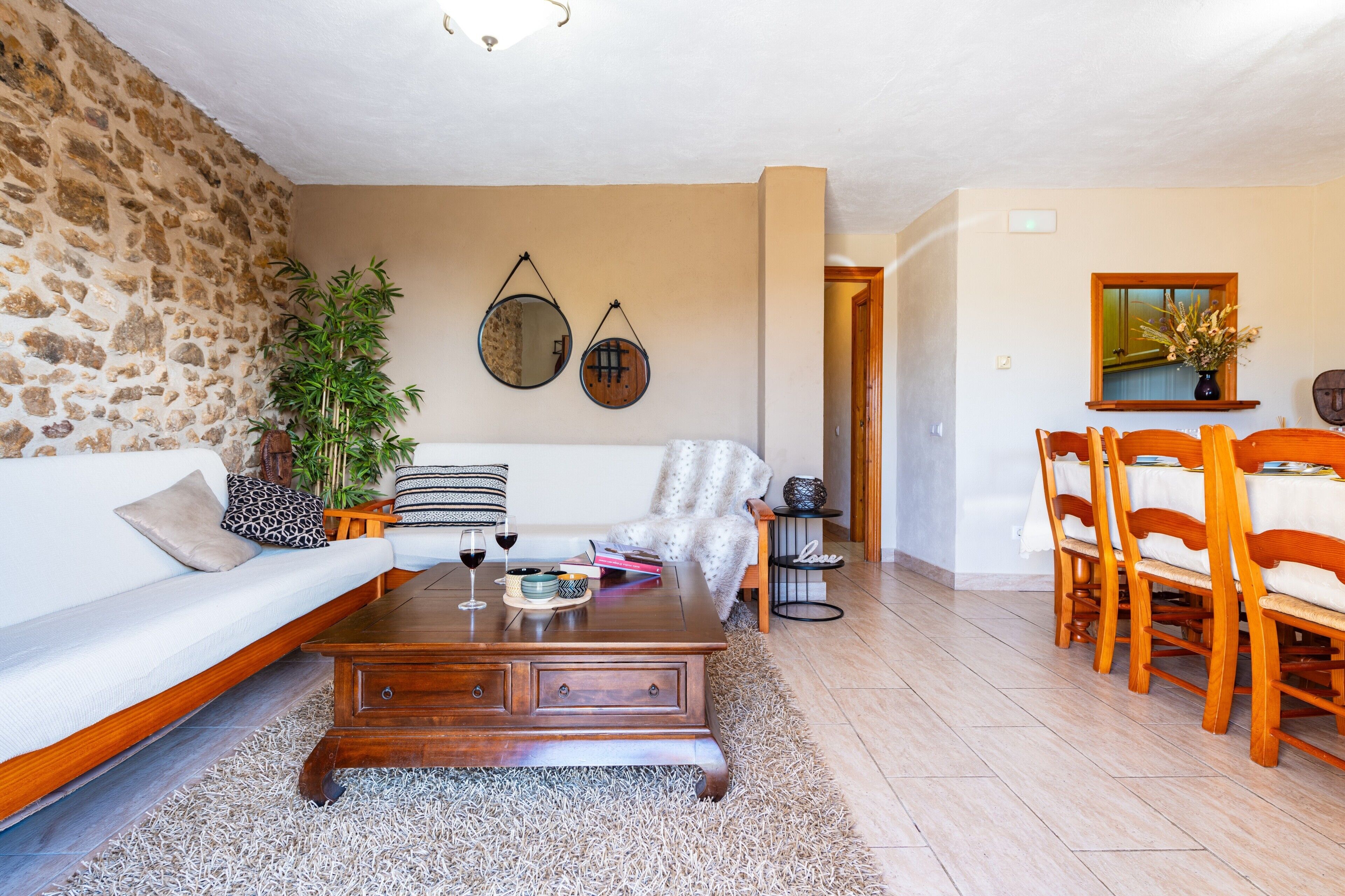 Un salon chaleureux avec un mur en pierre, un canapé en bois, une table basse et un coin repas comprenant des chaises et une table en bois.