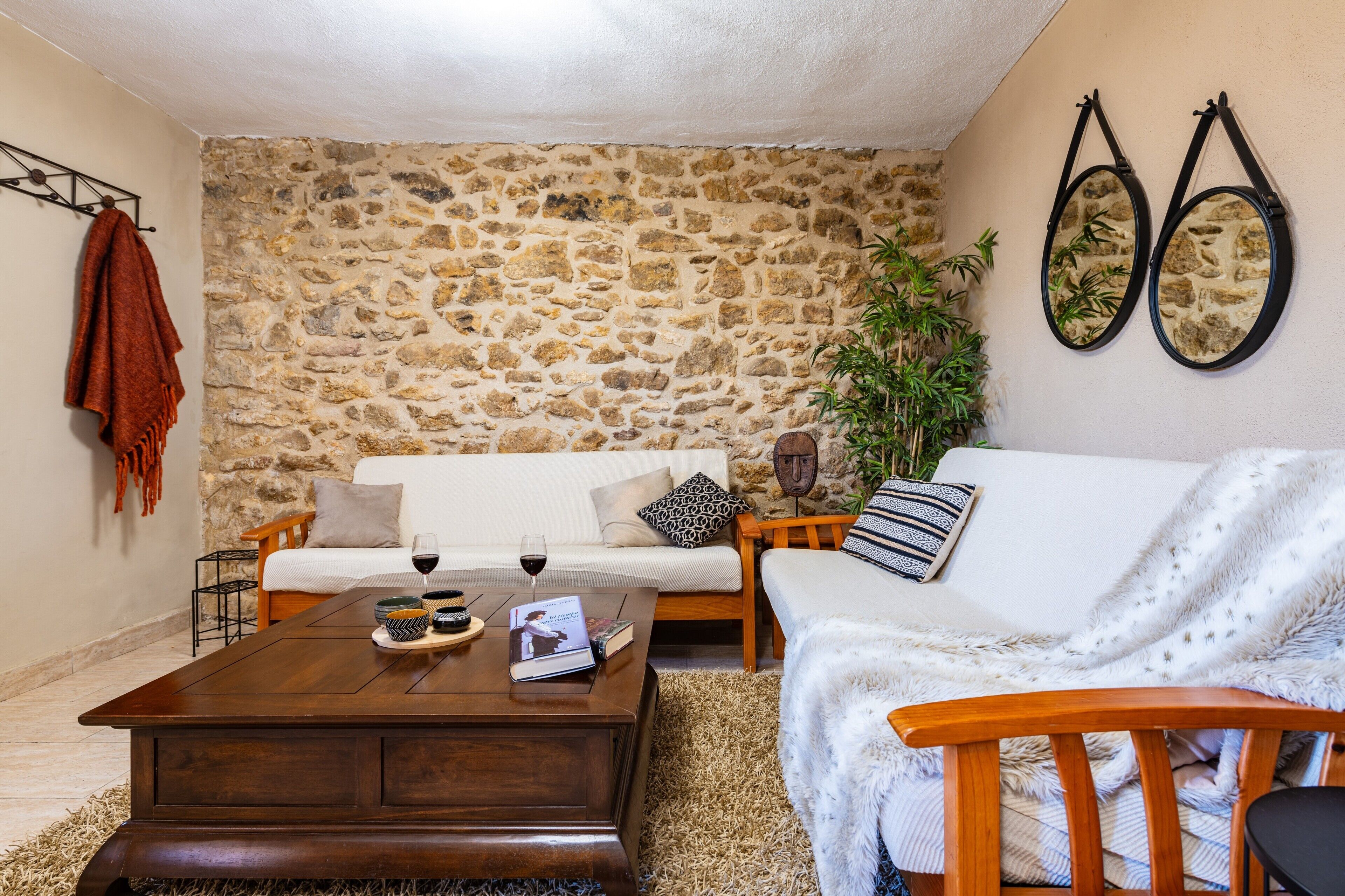 Una sala de estar acogedora con una pared de piedra, una mesa de centro de madera, un sofá blanco y una planta.
