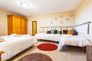 Quarto de hotel com duas camas, um guarda-roupa de madeira, um tapete vermelho e obras de arte decorativas na parede.