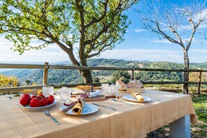 An outdoor dining table with food and drinks, surrounded by a scenic mountain view.