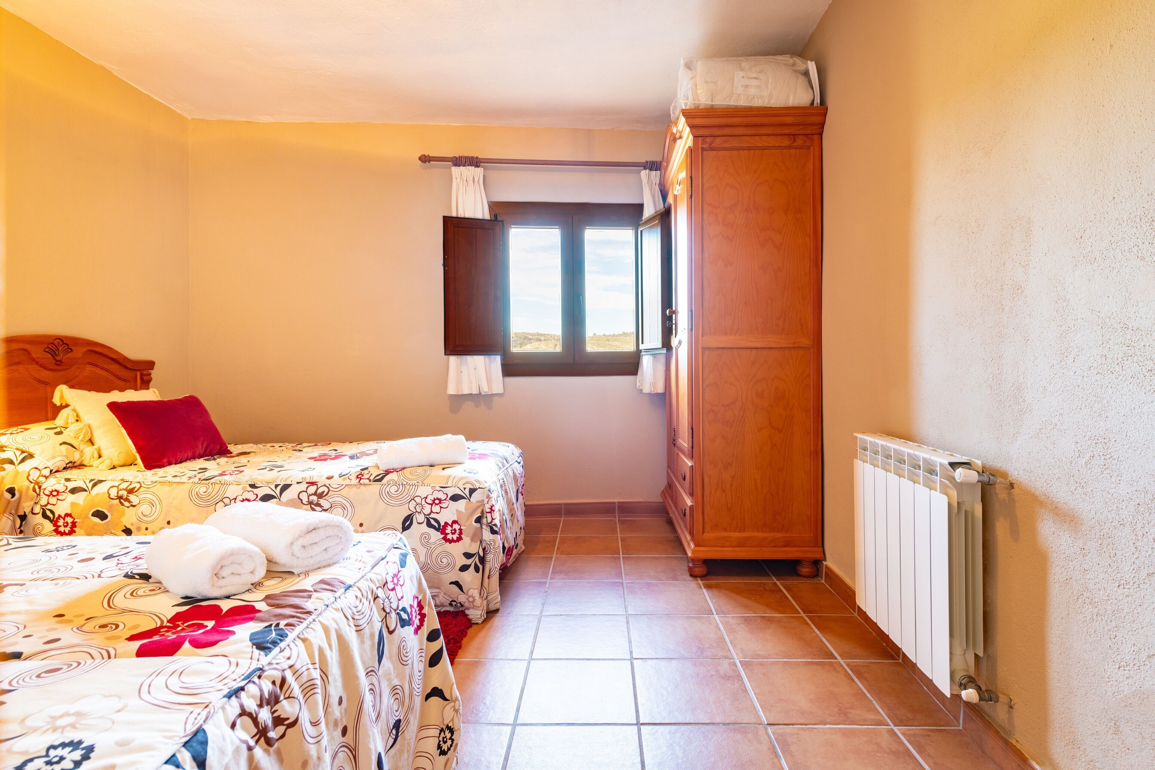 A bedroom with two beds, a wardrobe, a window, and a radiator.