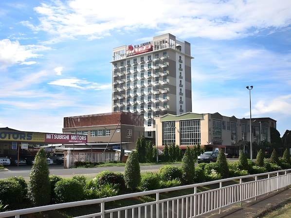 Un edificio de varios pisos con un letrero llamativo de Mitsubishi Motors, rodeado de vegetación y una cerca blanca.