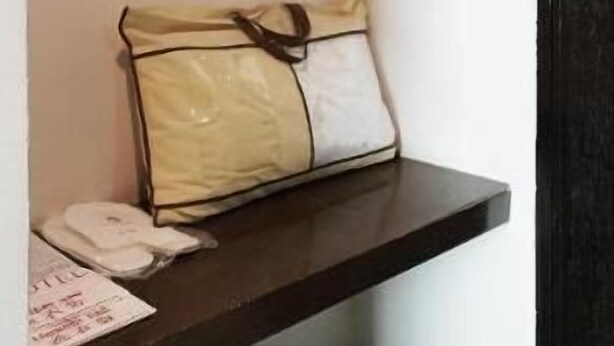 A small shelf with a beige and white bag, a white object, and a newspaper. - LA Hotel Tawau (Tawau)
