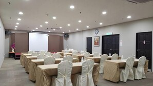 A conference room with tables and chairs, a projector screen, and a door with an exit sign. - LA Hotel Tawau (Tawau)