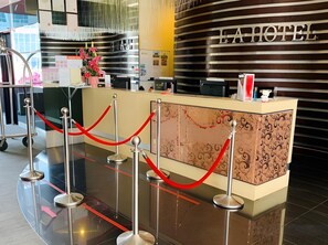 A hotel reception desk with a modern design, a red rope barrier, and a sign that reads 'E.A HOTEL'.
