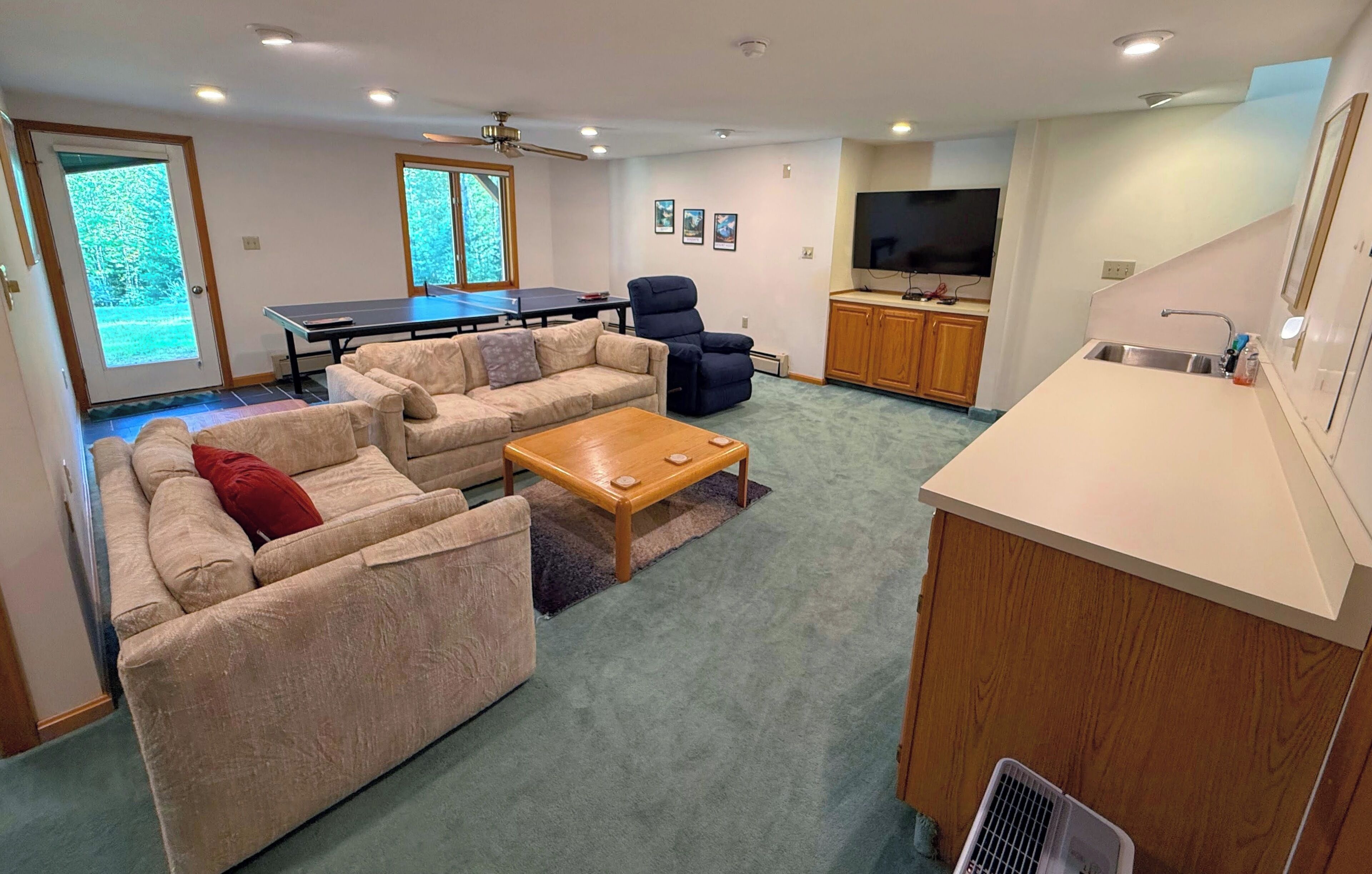 A living room with a sofa set, a coffee table, a ping pong table, a TV, and a kitchen area.