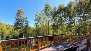 Une terrasse en bois avec une rambarde, deux chaises en bois et une vue sur une forêt.