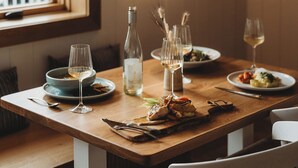 Una mesa de madera con platos de comida, copas de vino blanco y una botella de agua.