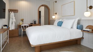 Un dormitorio con cama de madera, un escritorio con silla, un tocador con espejo y una mesita de noche con lámpara.