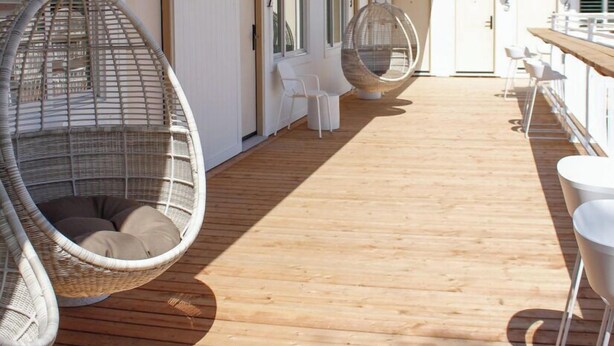 Una terraza de madera con sillas colgantes y un área de estar exterior blanca.