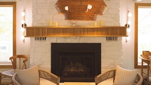 Una sala de estar acogedora con chimenea, dos sillones de mimbre, una mesa de centro de madera y un elemento decorativo de iluminación sobre la repisa.