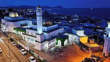 A mosque with a large dome and minarets, surrounded by a parking area and a coastal view.
