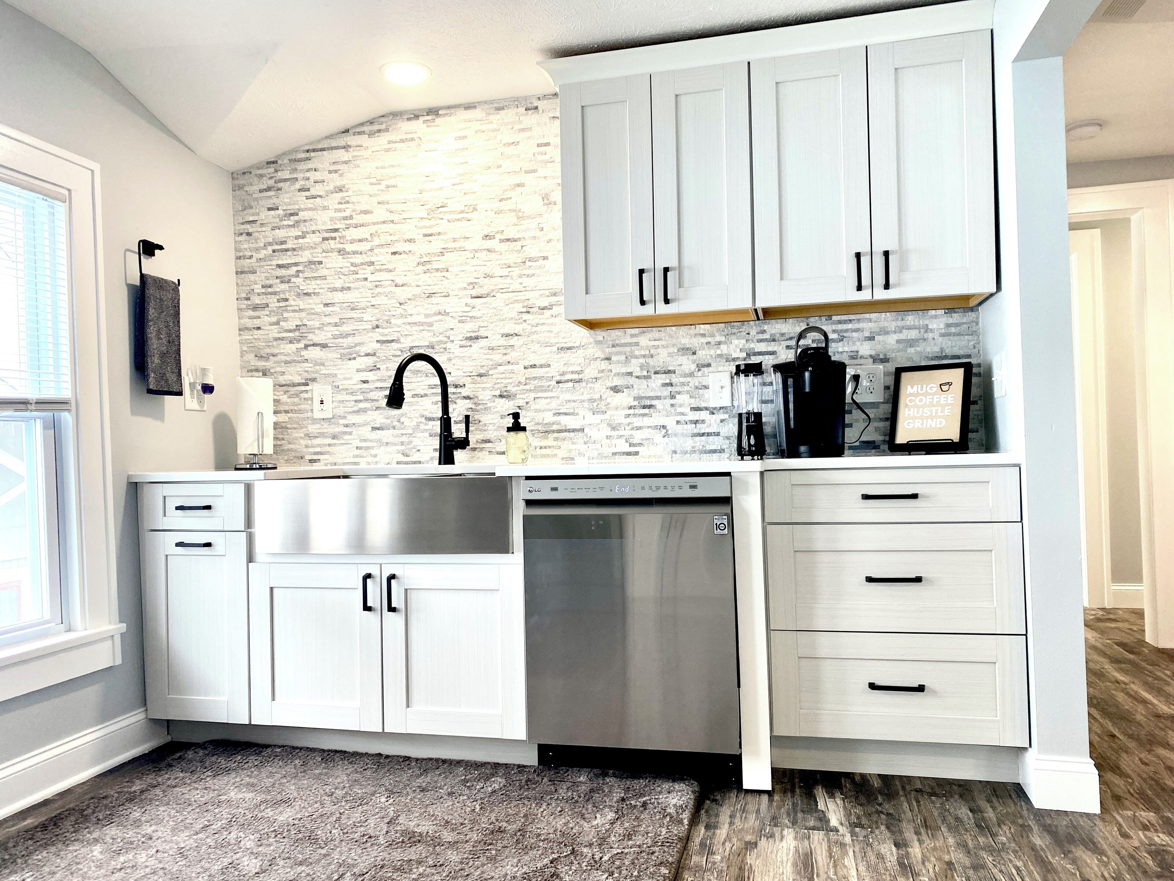 Una cocina moderna con armarios blancos, un lavamanos de acero inoxidable, lavavajillas y cafetera.