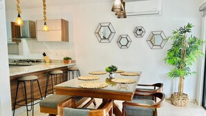 A modern kitchen with a dining area, featuring a central island, bar stools, and hexagonal mirrors on the wall. - Casa en privada frente a la alberca by PartnerHost (Mazatlán)