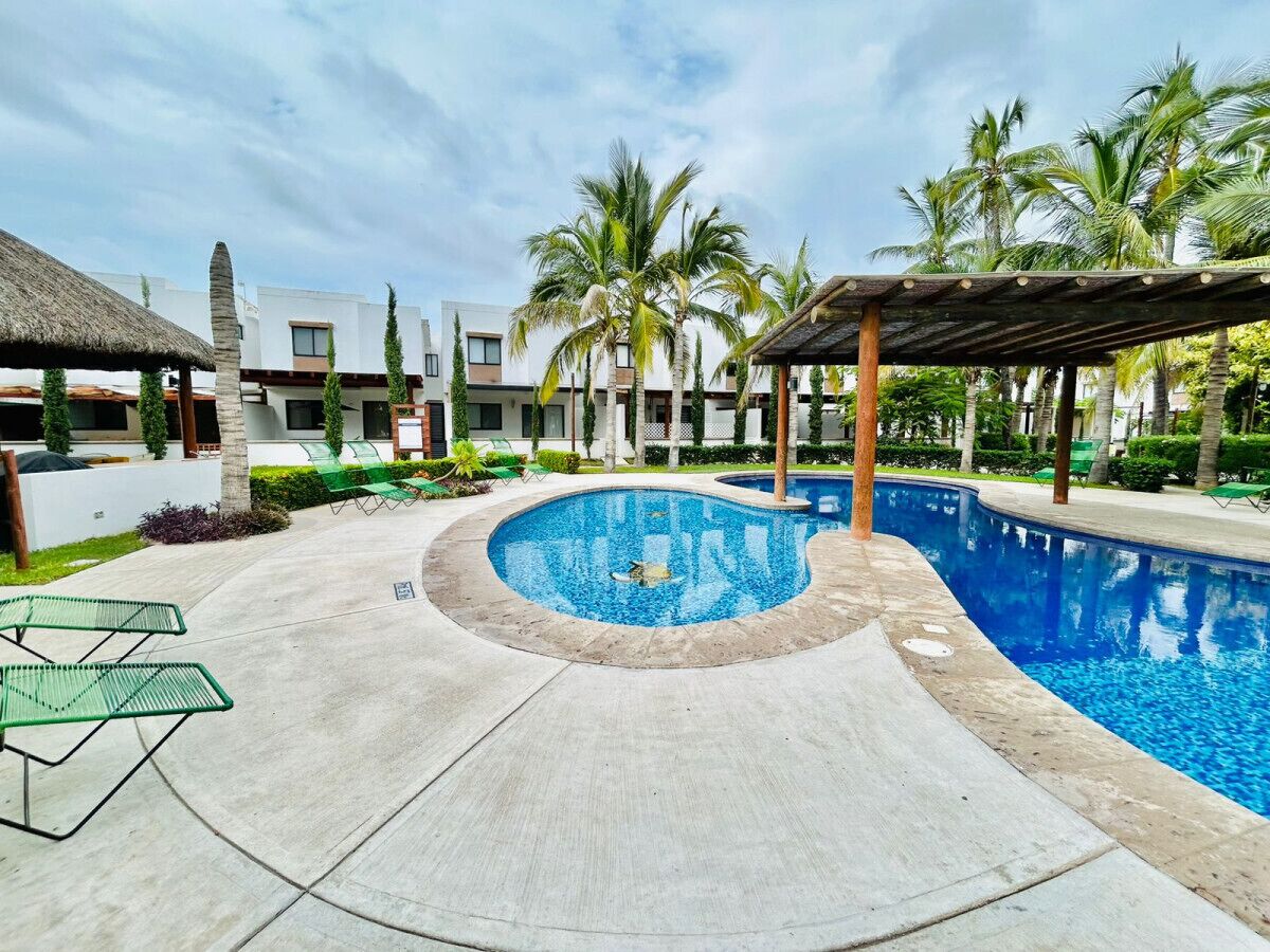 A swimming pool with a curved design, surrounded by a concrete deck and palm trees.