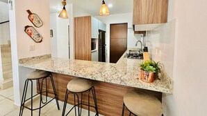 A kitchen with a granite countertop, wooden cabinets, and a central island with stools. - Casa en privada frente a la alberca by PartnerHost (Mazatlán)