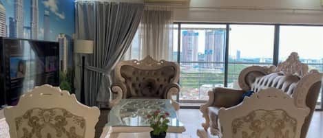Amplio salón con muebles ornamentados, una mesa de centro de vidrio y un gran ventanal con vista a la ciudad.