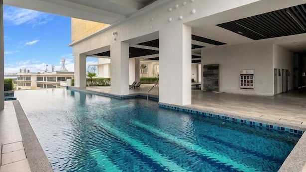 Une piscine à l’eau d’un bleu limpide, entourée d’une zone abritée avec des piliers blancs et un sol carrelé.