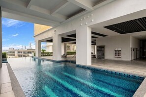 A swimming pool with a clear blue water, surrounded by a covered area with white pillars and a tiled floor. - Puchong Setiawalk Penthouse for 14 Pax Iconique (Puchong)