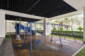 A playground with swings and a slide, surrounded by a covered area with a concrete floor. - Puchong Setiawalk Penthouse for 14 Pax Iconique (Puchong)