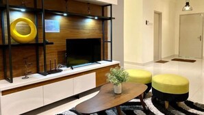 Un salon moderne avec un téléviseur à écran plat fixé à un mur en bois, une table basse et deux poufs jaunes.