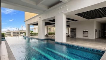 Una piscina con agua azul cristalina, rodeada por una zona techada con pilares blancos y piso de baldosas.