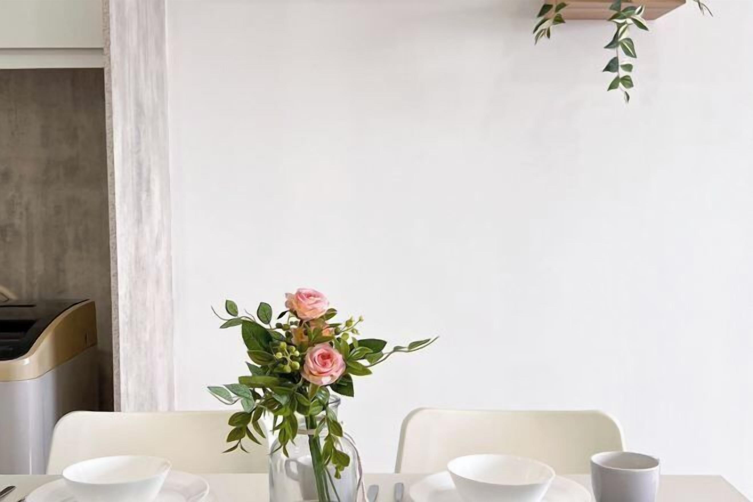 A dining table with white plates, bowls, and a cup, accompanied by a vase of pink flowers.