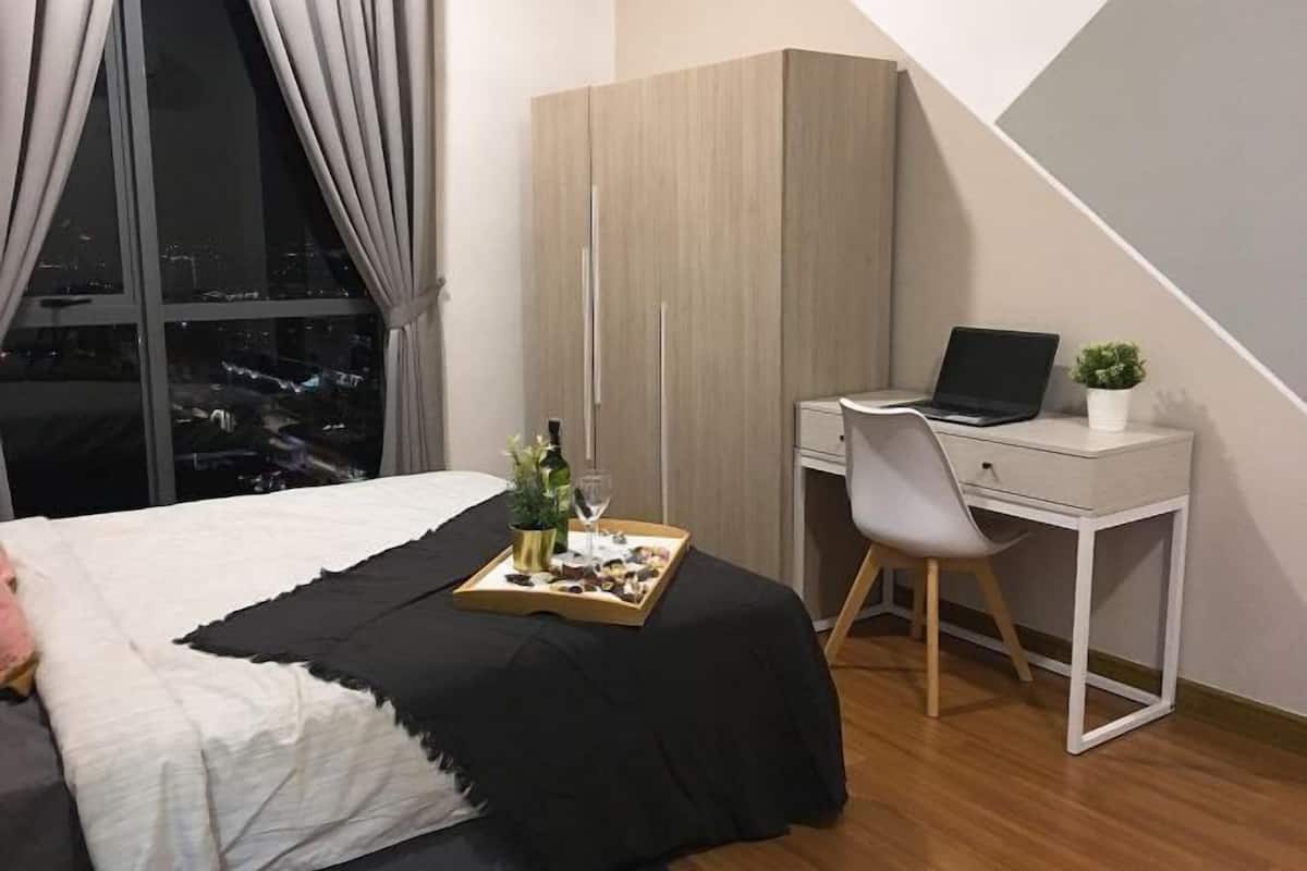 Ein modernes Schlafzimmer mit Bett, Schreibtisch mit Laptop, einer Ablage mit Snacks und Blick auf die Stadt durch das Fenster.