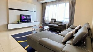Een moderne woonkamer met een bank, een salontafel, een aan de muur bevestigde televisie en een groot raam met gordijnen.