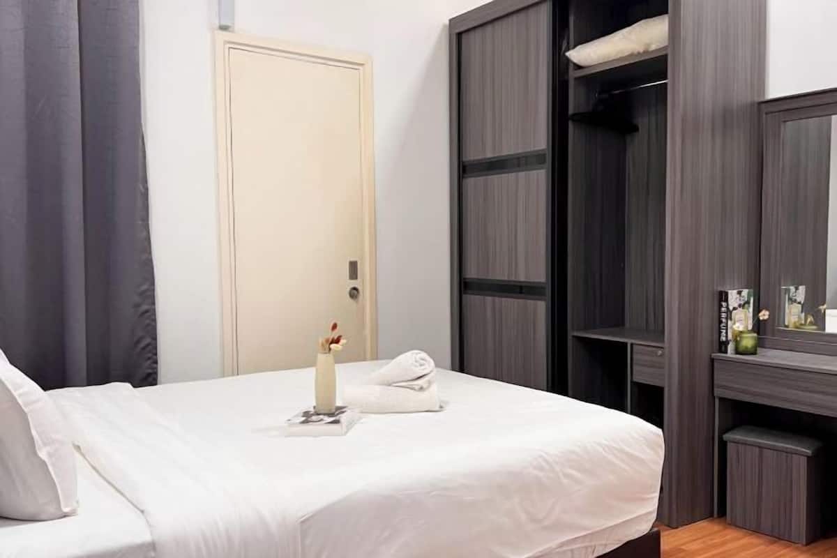 Ein ordentlich bezogenes Bett mit weißer Decke, einem Handtuch und einer Vase mit Blumen. Eine Tür und ein Kleiderschrank mit Spiegel sind ebenfalls vorhanden.
